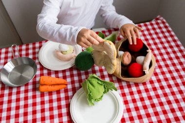 Kırmızı kareli masa örtüsünde oyuncak sebzelerle oynayan çocuk.