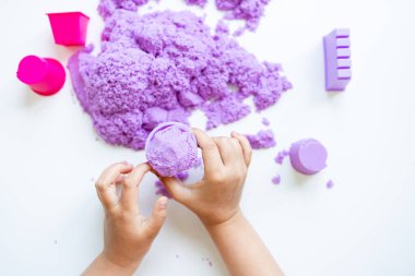 Beyaz arka planda mor kinetik kum ve küflerle oynayan çocuk elleri. Yüksek kalite.