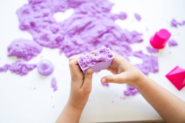 Beyaz yüzeyde mor kinetik kumla oynayan bir çocuk. Yüksek kalite.