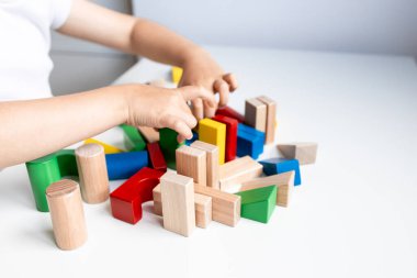 Beyaz yüzeyde renkli geometrik tahta bloklarla oynayan bir çocuk. Yüksek kalite.