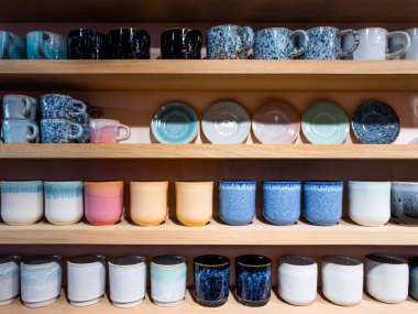 Renkli seramik bardaklar ve kupalar ahşap raflarda sergileniyor. Yüksek kalite.