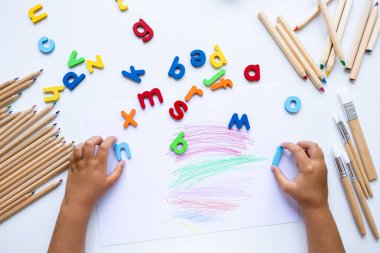 Çocuk renkli harfler ve pastel boyalarla yaratıcı alfabe öğrenme işine girmiş. Yüksek kalite.