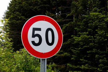 Yeşillik ağaçlar arasında saatte 50 km hız sınırı işareti. Yüksek kalite.