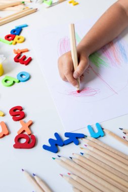 Beyaz yüzeye renkli kalemler ve alfabe harfleri çizen çocuk. Yüksek kalite.