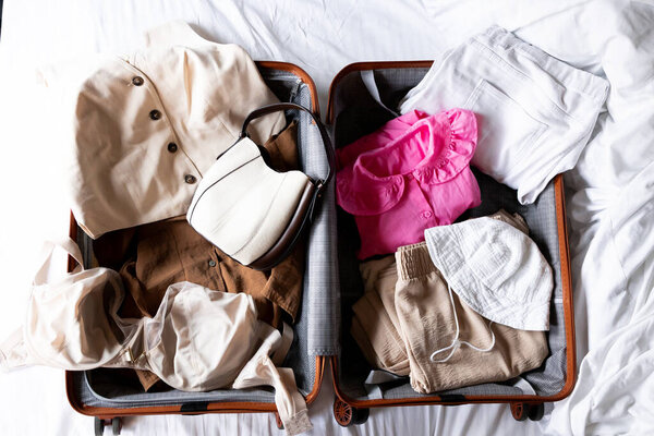 Открытый чемодан с повседневной одеждой и аксессуарами на кровати. Высокое качество.