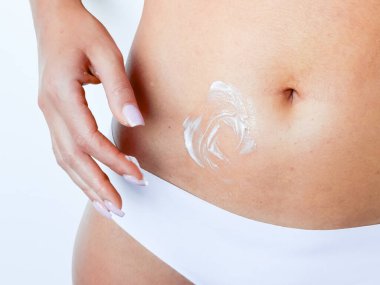 Kadın mide üzerine nemlendirici krem sürüyor. Yüksek kalite.