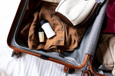 Giysilerle dolu bavul, tuvalet malzemeleri ve seyahate ya da tatile hazır şapka. Yüksek kalite.