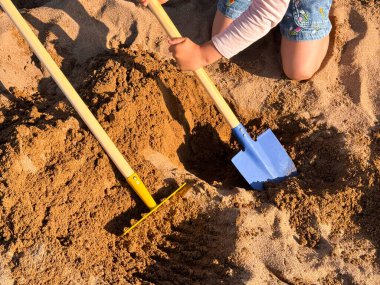 Güneşli bir sahil gününde parlak renkli küreklerle kumda oynayan bir çocuk. Yüksek kalite.