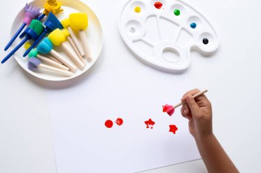 Child creating colorful art with paintbrushes and palette on white paper. High quality.