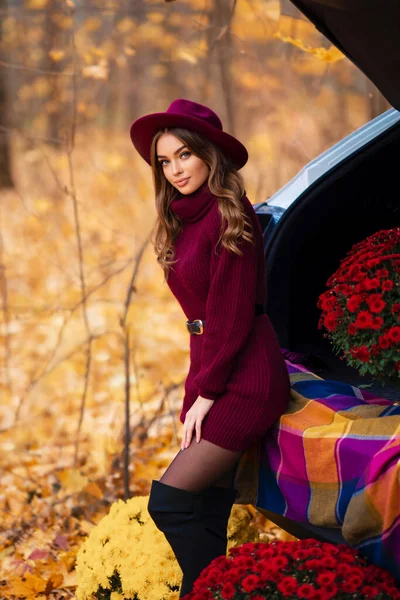 穿着舒适的针织勃艮第服装 头戴帽子的漂亮姑娘坐在车上 有着秋天的背景 — 图库照片