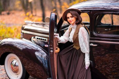 Eski moda elbiseli, dantel bluzlu ve peçeli güzel bir kadın sonbahar arka planında retro kahverengi arabada oturuyor. Eldiven giymiş zarif bir bayan. Sıcak sanat eserleri..
