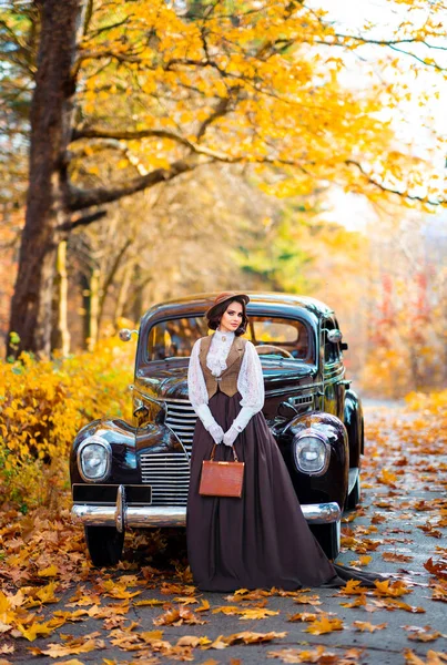 秋の背景にレトロな茶色の車の近くに立ってベールとヴィンテージのドレス レースブラウスと帽子の美しい女性 自然の上にポーズをとる手袋のエレガントな女性暖かい芸術作品 — ストック写真