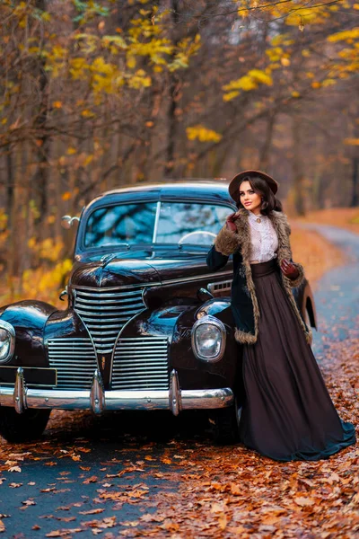 秋の背景にレトロな茶色の車の近くに立ってベールとヴィンテージのドレス レースブラウスと帽子の美しい女性 自然の上にポーズをとる手袋のエレガントな女性暖かい芸術作品 — ストック写真