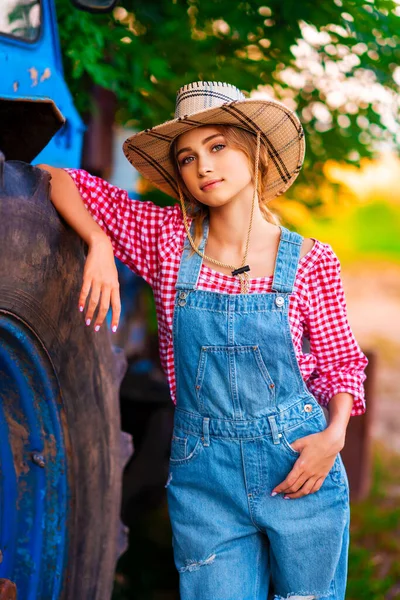 Piękna Blondynka Kowbojka Słomkowym Kapeluszu Dżinsach Stojąca Pobliżu Niebieskiego Ciągnika — Zdjęcie stockowe