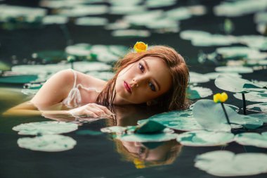 Beautiful red haired girl in white dress posing in river with water lilies. Fairytale story about  ophelia .Warm art work