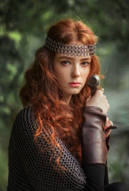 Ortaçağ metal zırhlı güzel kızıl saçlı kız. Kılıcı savaş pozisyonunda duruyor. Savaşçı hakkında bir masal. Sıcak sanat eserleri.