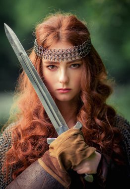 Beautiful red haired girl in metal medieval armor dress with sword standing in warlike pose. Fairy tale story about warrior . Warm art work. clipart