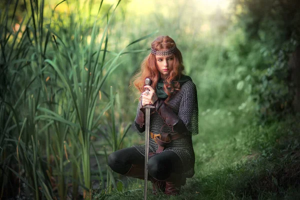 漂亮的红头发姑娘穿着中世纪金属盔甲 剑拔弩张地站在那里 关于战士的童话故事 温暖的艺术作品 — 图库照片