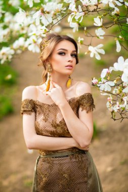 Çiçek açan bahçede dikilen dantelli kahverengi elbiseli güzel romantik kız. Manolya ağaçları arasında genç bir model hayal ediyorum..