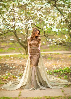 Çiçek açan bahçede dikilen dantelli kahverengi elbiseli güzel romantik kız. Manolya ağaçları arasında genç bir model hayal ediyorum..