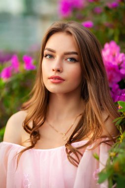 Renkli çiçeklerin yanında duran pembe klasik elbiseli ve hasır şapkalı güzel kız. Romantik bir kadının sanat eseri. Sevimli bir model, poz veriyor ve kameraya bakıyor..