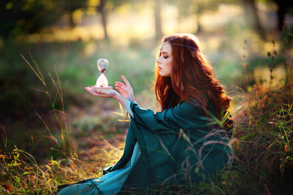 Portrait of a beautiful red haired girl in green medieval dress on glowing sun. Fairy tale story about brave heart woman.Amazing model looking at camera.Warm art work