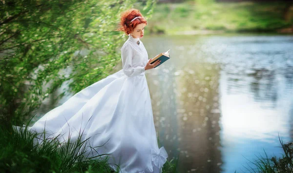 美しい赤髪の少女白い長いヴィンテージドレス本と川の近くに立っています レース傘とロマンチックな女性のアートワーク — ストック写真