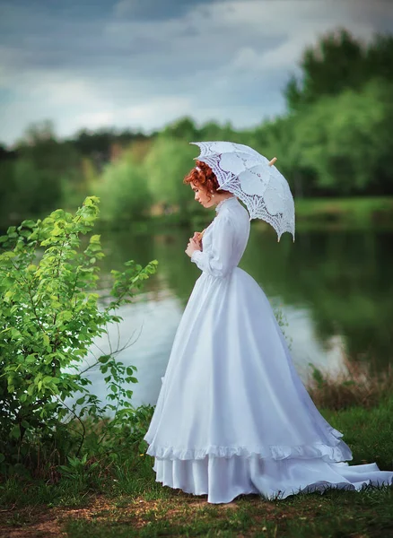 穿着白色长衫站在河边的美丽的红头发姑娘 带着花边伞的浪漫女人的艺术作品 — 图库照片