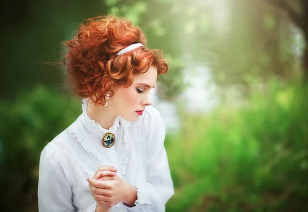 美丽的红头发姑娘 身穿白色的长衫 坐在河边的草地上 一个带着书和花边伞的浪漫女人的艺术作品 — 图库照片