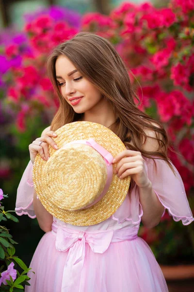 ピンクのヴィンテージドレスとカラフルな花の近くに立っているわらの帽子の美しい女の子 ロマンチックな女性のアート作品かなり優しさモデルポーズとカメラを見て — ストック写真
