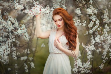 Spring Beautiful romantic red haired girl in white  lace dress standing in blooming garden. Dreaming young model looking down. clipart