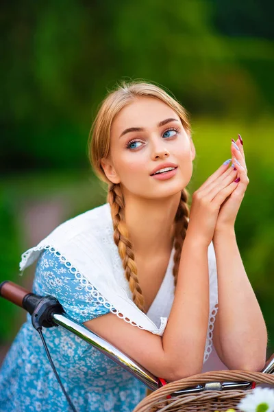 美丽的金发碧眼的年轻姑娘 穿着蓝色的短裙 站在白色的自行车旁边 一篮束巨大的菊花 — 图库照片