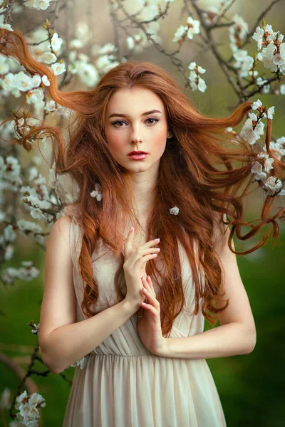 春開花庭に立って白いレースのドレスで美しいロマンチックな赤い髪の女の子 若いモデルを夢見てカメラを見て — ストック写真