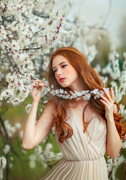 Spring Beautiful romantic red haired girl in white  lace dress standing in blooming garden. Dreaming young model looking afar.