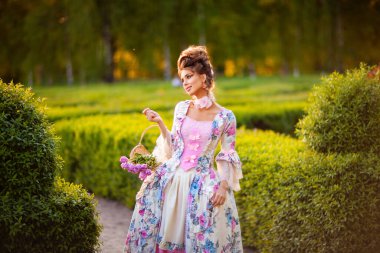 Baharda mükemmel saç stili olan güzel romantik kız elinde çiçeklerle yeşil bahçede dikiliyor. Peri masalı gibi giyinmiş rüya kraliçesi. Peri masalı gibi..