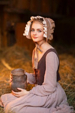 Ortaçağ elbisesi ve şapka takmış, bir sürahi sütle çiftlikte poz veren güzel, kırsal bir kız. Kırsal kesimde güzel sarışın bir manken.. 
