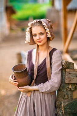 Ortaçağ elbisesi ve şapka takmış, bir sürahi sütle çiftlikte poz veren güzel, kırsal bir kız. Kırsal kesimde güzel sarışın bir manken.. 