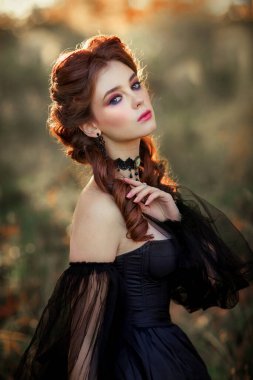 Sonbahar ağacının yanında duran muhteşem moda gotik kız portresi. Fantezi sanat çalışmaları. Siyah elbiseli ve şapkalı kızıl saçlı manken kamera ve pozlara bakıyor. 
