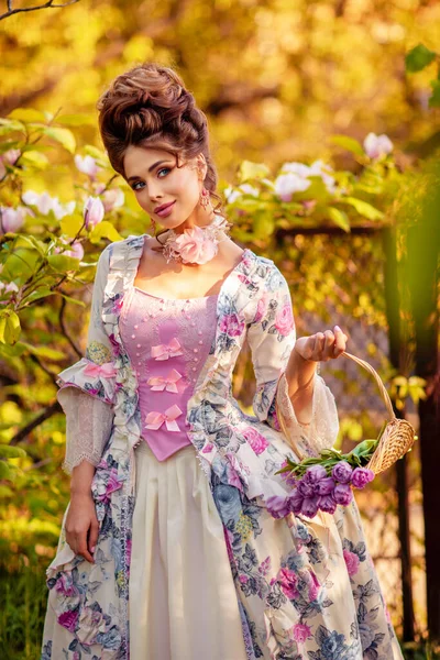 春花のバスケットとモクレンの庭の開花に立って完璧な髪型を持つ美しいロマンチックな女の子 妖精の美しいヴィンテージドレスのポーズで女王を夢見ます — ストック写真
