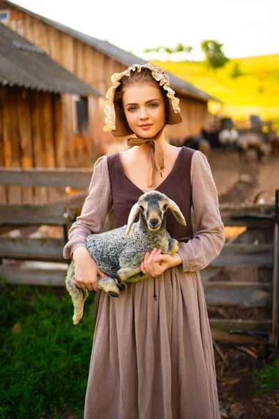 stock image Beautiful young rural girl in medieval dress and bonnet hat posing on a ranch. Pretty blonde model in countryside art photo. 