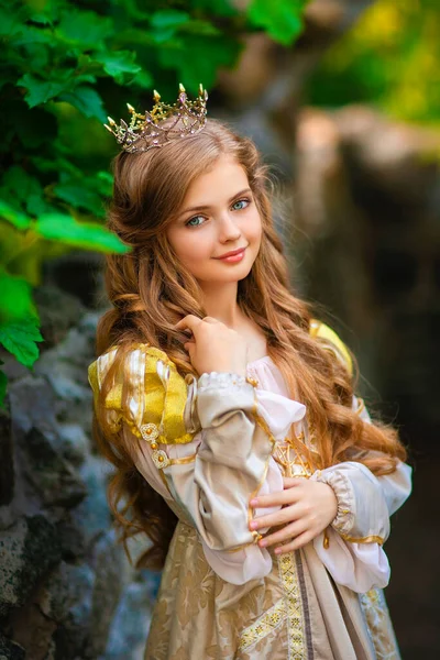 黄金の中世のドレスと小さな王冠の美しい若いブロンドの王女 美しい女王は石城の近くにポーズをとっています — ストック写真