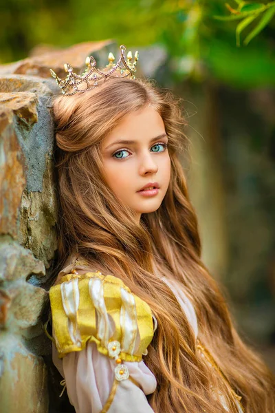 美丽的金发碧眼的公主穿着中世纪金色的衣服 头戴小小的皇冠 漂亮的女王在石碑旁边摆姿势 温暖的艺术作品 — 图库照片