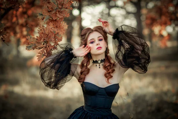 秋の木の近くに立つ壮大なファッションゴシックガールの肖像 ファンタジーアート作品黒のドレスと帽子の素晴らしい赤い髪のモデルは カメラとポーズを見ています — ストック写真