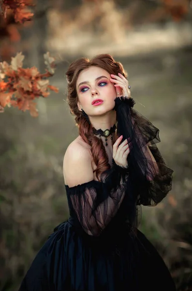 秋の木の近くに立つ壮大なファッションゴシックガールの肖像 ファンタジーアート作品黒のドレスと帽子の素晴らしい赤い髪のモデルは カメラとポーズを見ています — ストック写真