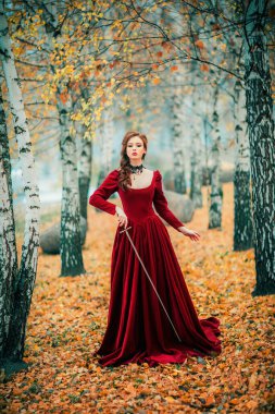 Sonbahar ormanlarında dikilen muhteşem moda gotik kız portresi. Fantezi sanatı. Kılıçlı kırmızı saçlı manken.. 