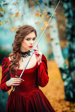 Sonbahar ormanlarında dikilen muhteşem moda gotik kız portresi. Fantezi sanatı. Kılıçlı kırmızı saçlı manken.. 