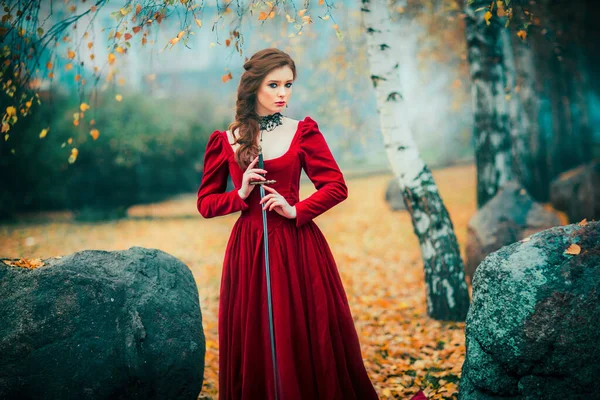 秋の森の中に立つ壮大なファッションゴシックガールの肖像 ファンタジーアート作品剣でクラレットドレスの素晴らしい赤い髪のモデル若い姫戦士についてのおとぎ話 — ストック写真