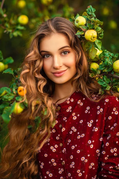 一个卷曲长发的画像 漂亮的女孩穿着红色天鹅绒衣服 披着披风在苹果园里摆姿势 浪漫女人的艺术作品 看着相机的漂亮柔情模型 — 图库照片