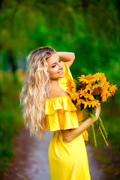 漂亮的金发姑娘穿着黄色的衣服 享受大自然 快乐地微笑着站在绿树成荫的女性 温暖的照片 艺术品 — 图库照片