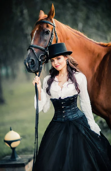 华丽的时尚哥特式女骑着马的画像 幻想的艺术作品和华丽的色彩 黑白裙和帽子造型的迷人的黑发模特 — 图库照片